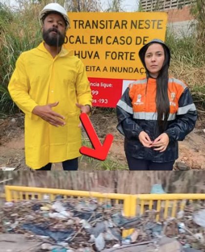 Dois agentes com capas de chuva diante de uma placa de alerta e de entulho retirado de um córrego.
